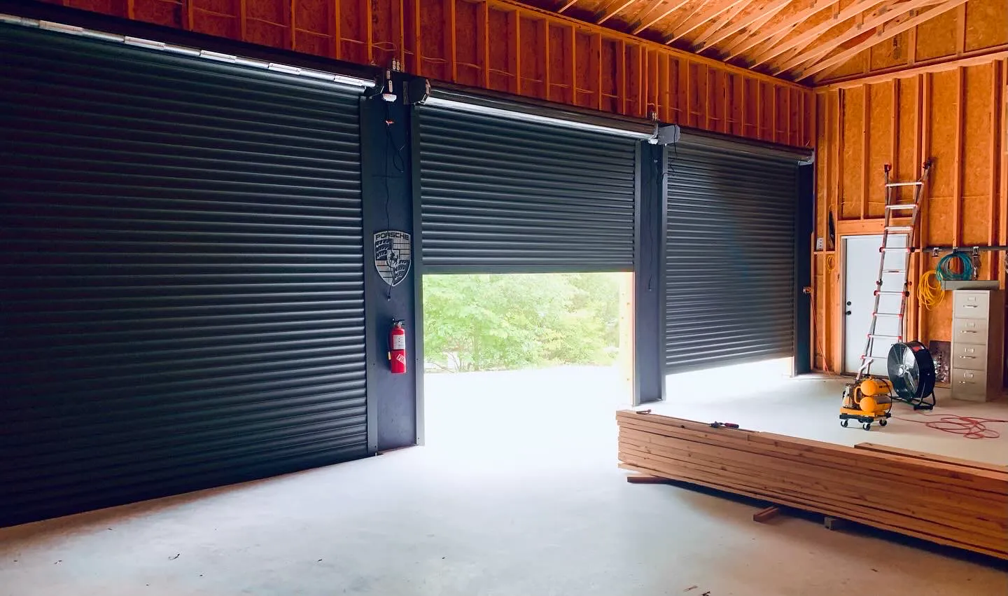 Three black TMAX roll-up garage doors viewed from inside a wood-framed garage